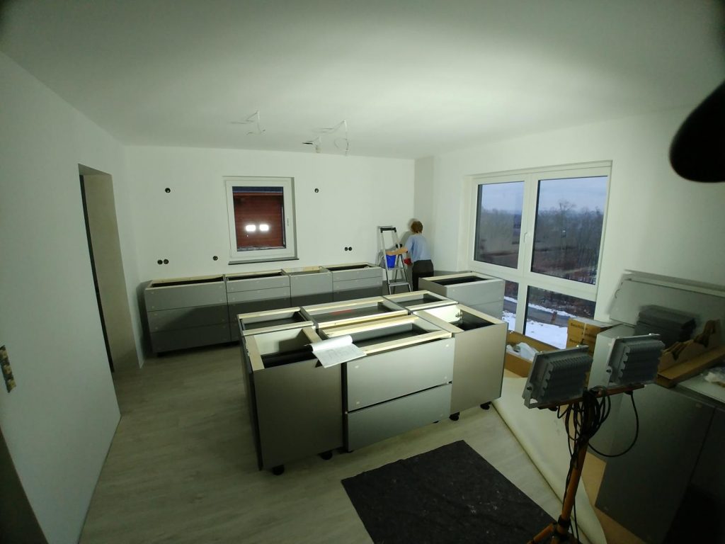 Vorne sieht man die Kücheninsel, in die ein 90cm breiter Induk-Herd eingebaut wird. Hinten an der Wand ist der zukünftige Arbeitsbereich mit einem Spülbecken unter dem Fenster.